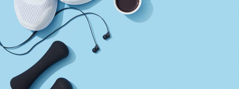 Sports equipment and accessories, shoes, dumbbells, earphones and coffee on blue background